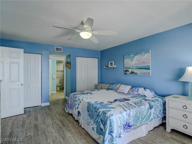 bedroom featuring hardwood / wood-style flooring, ensuite bathroom, ceiling fan, and two closets