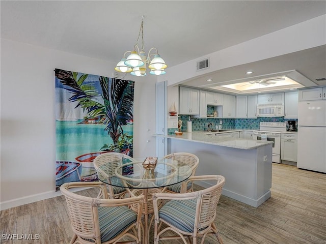 dining space featuring an inviting chandelier, a tray ceiling, sink, and light wood-type flooring