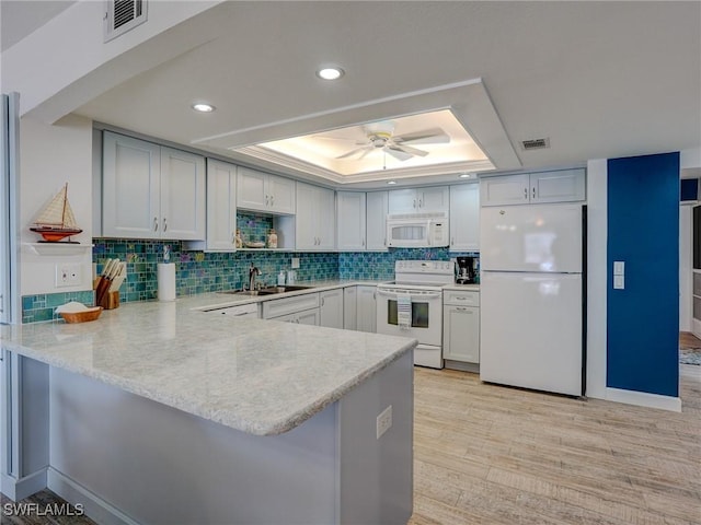 kitchen featuring sink, white appliances, light hardwood / wood-style flooring, a tray ceiling, and kitchen peninsula