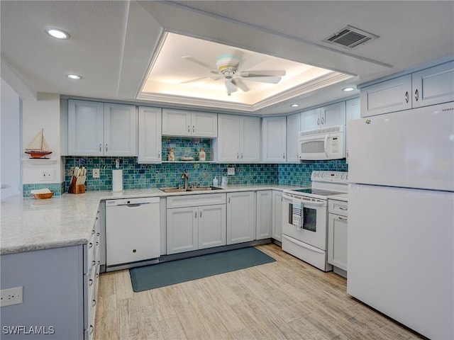 kitchen featuring a tray ceiling, sink, white appliances, and light hardwood / wood-style floors