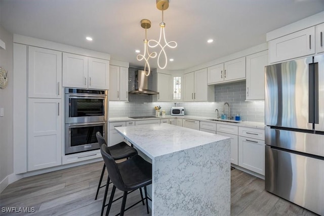 kitchen featuring white cabinets, decorative backsplash, stainless steel appliances, wall chimney range hood, and a sink