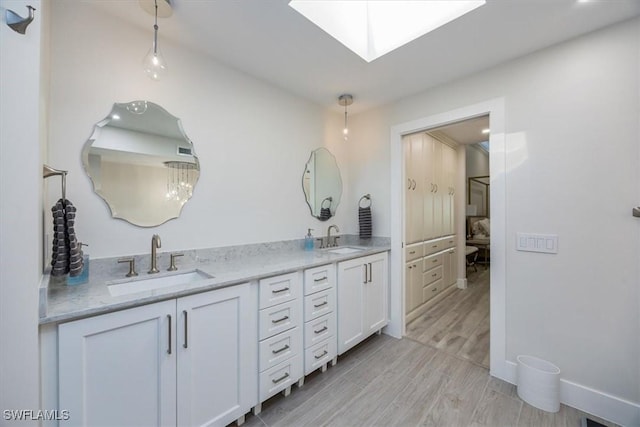 full bathroom with double vanity, wood finished floors, a skylight, and a sink