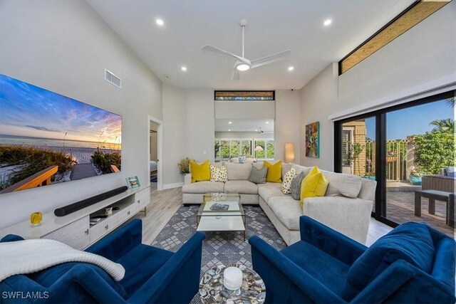 living room featuring ceiling fan, a towering ceiling, and light wood-type flooring