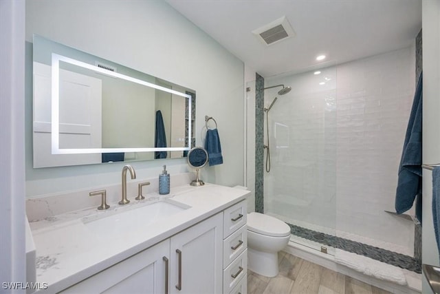 bathroom with toilet, wood finished floors, vanity, visible vents, and a stall shower