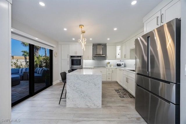 kitchen with wall chimney range hood, tasteful backsplash, white cabinetry, and stainless steel appliances