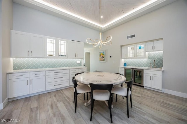 dining area featuring light wood-style floors, a tray ceiling, beverage cooler, and visible vents