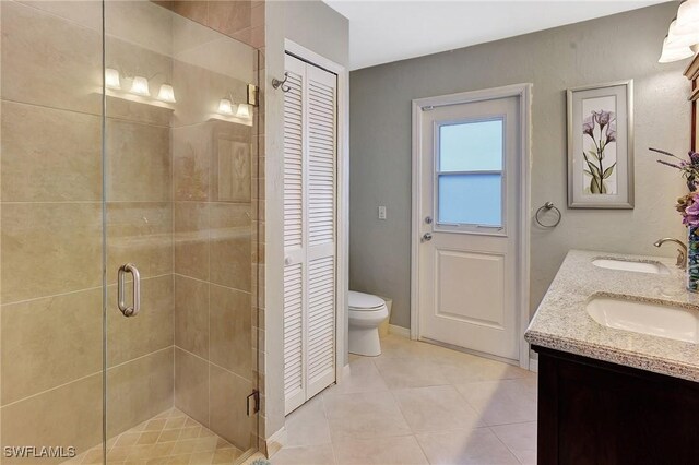 bathroom with a shower with door, vanity, tile patterned floors, and toilet