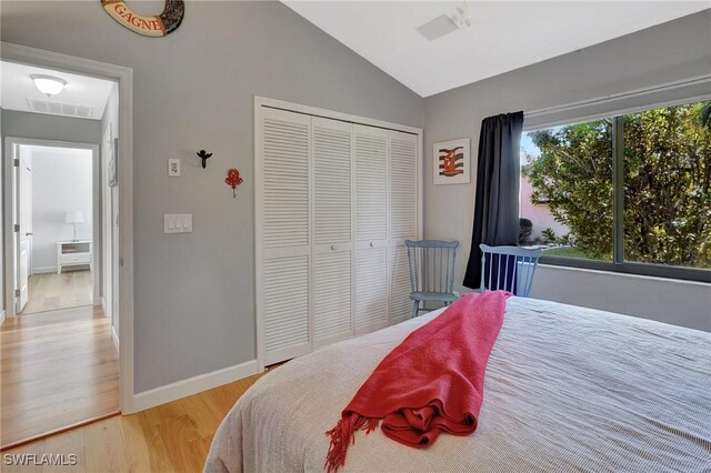 bedroom featuring light hardwood / wood-style floors, vaulted ceiling, and a closet