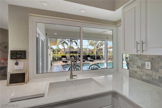 kitchen with white cabinetry, light stone countertops, sink, and decorative backsplash