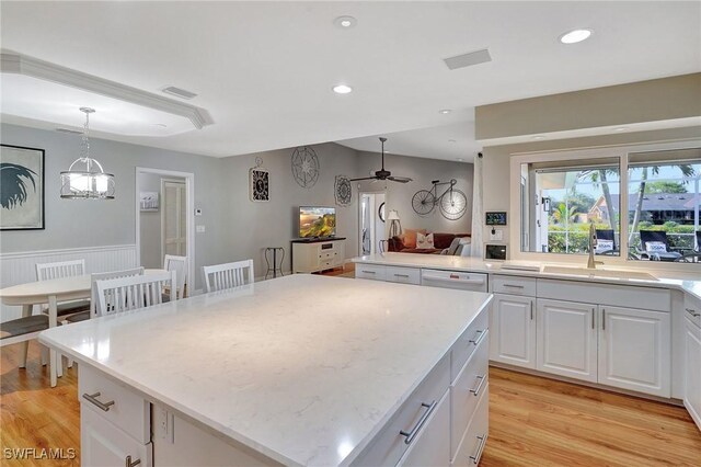 kitchen featuring decorative light fixtures, white cabinetry, sink, a center island, and light wood-type flooring