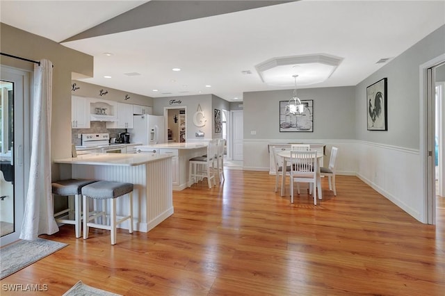 kitchen featuring a breakfast bar area, decorative light fixtures, kitchen peninsula, white appliances, and white cabinets