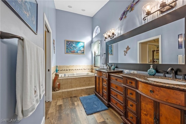 bathroom with vanity, a relaxing tiled tub, and wood-type flooring