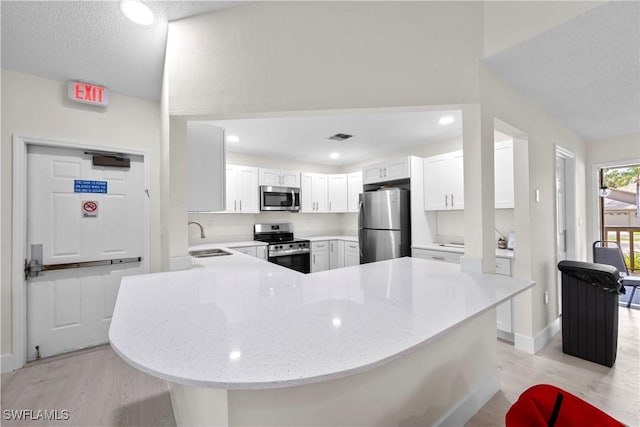 kitchen featuring sink, appliances with stainless steel finishes, light stone countertops, white cabinets, and kitchen peninsula