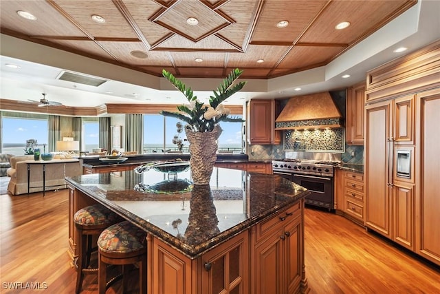 kitchen with dark stone countertops, premium appliances, a large island, wood ceiling, and custom range hood