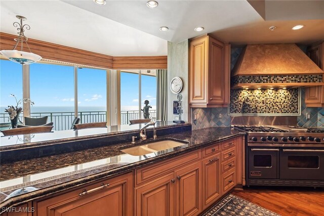 kitchen featuring sink, a water view, custom range hood, dark stone counters, and range with two ovens