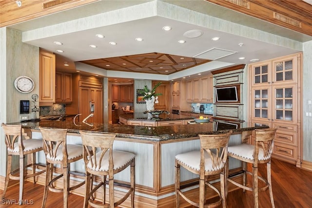 kitchen with dark stone countertops, a kitchen bar, kitchen peninsula, and paneled built in refrigerator