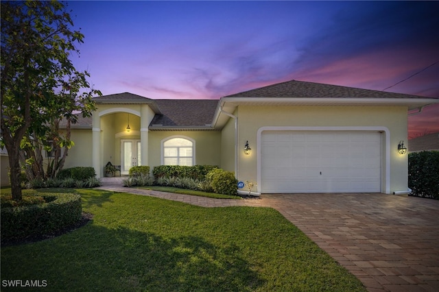 view of front of home featuring a garage, a yard, decorative driveway, roof with shingles, and stucco siding