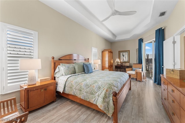 bedroom with light wood finished floors, access to outside, a tray ceiling, and visible vents