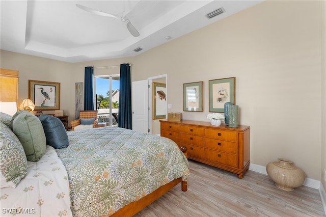 bedroom with access to exterior, a tray ceiling, visible vents, light wood-style floors, and baseboards