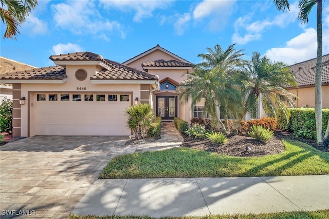 mediterranean / spanish-style house featuring decorative driveway, french doors, an attached garage, and stucco siding