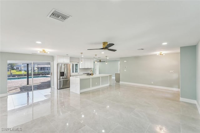 kitchen featuring stainless steel fridge, a center island with sink, visible vents, open floor plan, and white cabinetry