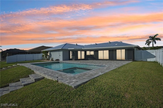 back of property at dusk with a patio, a fenced backyard, metal roof, an in ground hot tub, and a yard