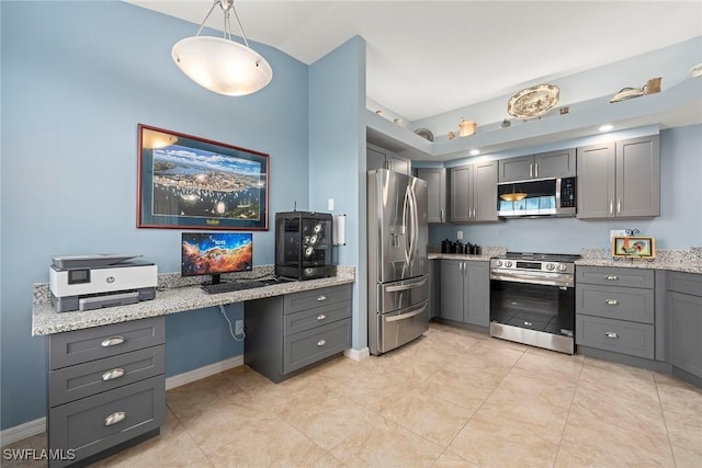 kitchen with gray cabinets, stainless steel appliances, light stone counters, built in desk, and decorative light fixtures