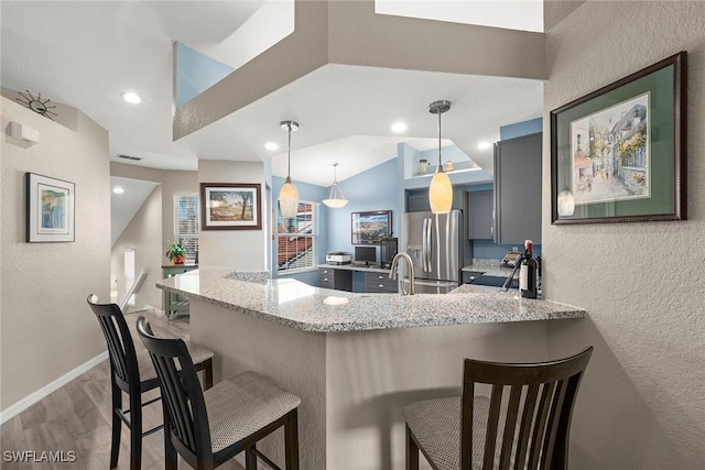 kitchen featuring pendant lighting, a breakfast bar area, light stone counters, kitchen peninsula, and stainless steel refrigerator with ice dispenser