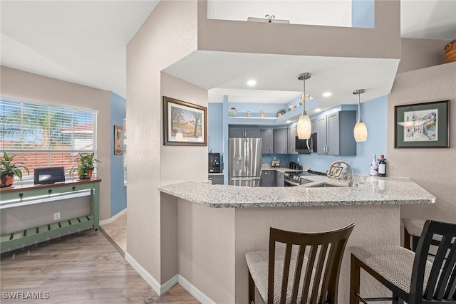 kitchen with sink, appliances with stainless steel finishes, light stone countertops, decorative light fixtures, and kitchen peninsula