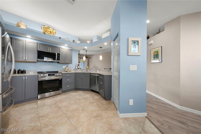 kitchen with gray cabinetry, light stone counters, decorative light fixtures, appliances with stainless steel finishes, and kitchen peninsula