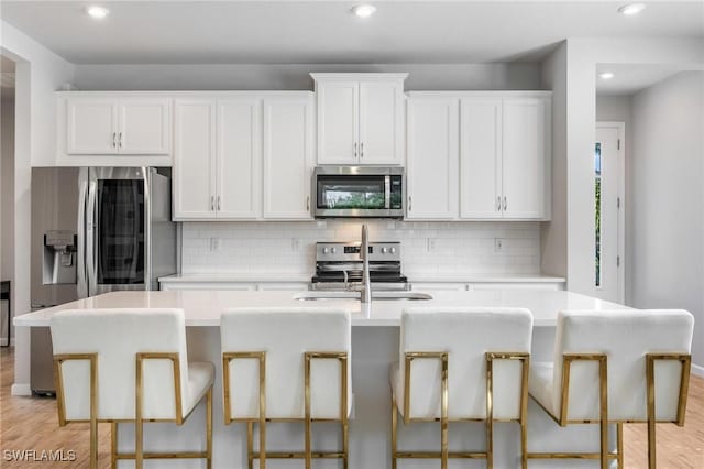 kitchen featuring a center island with sink, a kitchen breakfast bar, white cabinets, and appliances with stainless steel finishes