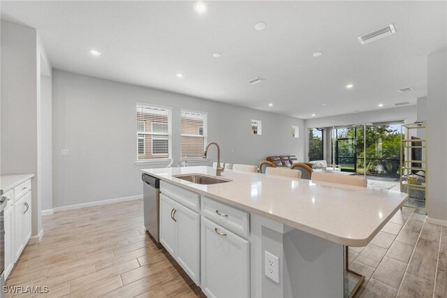 kitchen featuring sink, white cabinetry, a center island with sink, a kitchen bar, and stainless steel dishwasher