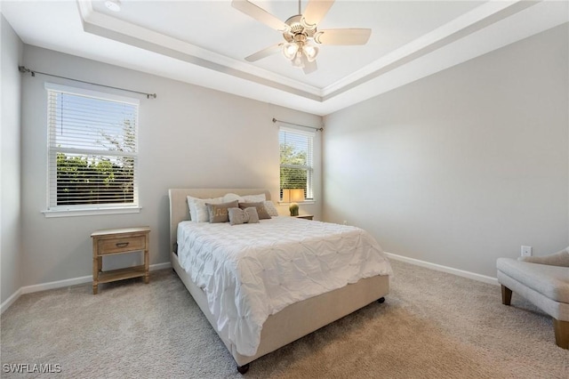 bedroom with light carpet, ceiling fan, and a tray ceiling