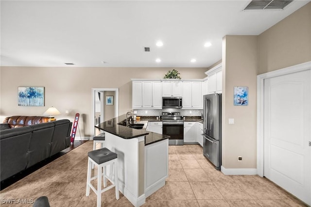 kitchen with sink, appliances with stainless steel finishes, white cabinets, a kitchen bar, and decorative backsplash