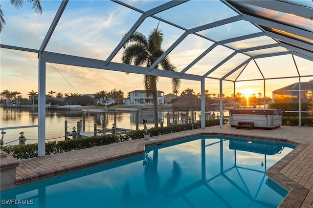 pool at dusk featuring a water view, a hot tub, a patio area, and glass enclosure