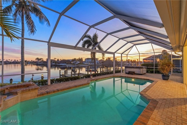 pool at dusk featuring a hot tub, a patio, a water view, and glass enclosure