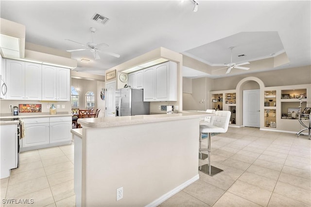 kitchen with built in features, white cabinetry, stainless steel fridge, ceiling fan, and a tray ceiling