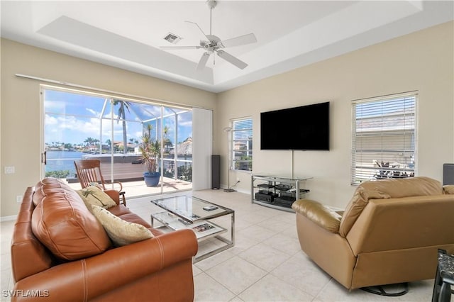 tiled living room featuring a tray ceiling, ceiling fan, and a water view