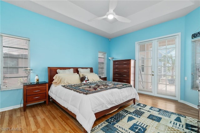 bedroom with multiple windows, a tray ceiling, access to outside, and light hardwood / wood-style flooring