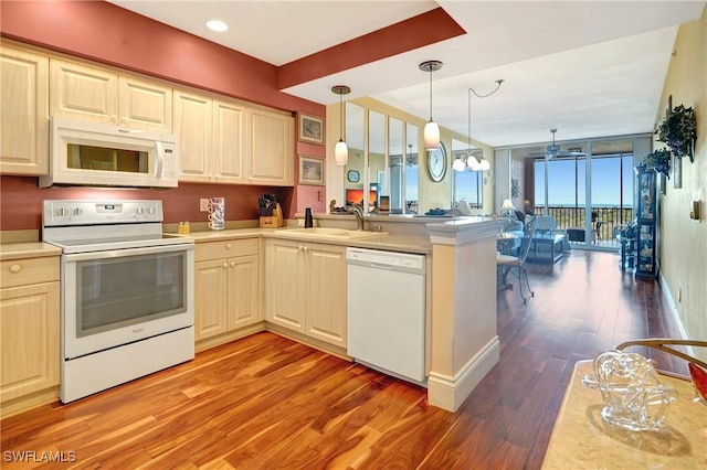 kitchen with pendant lighting, sink, white appliances, wood-type flooring, and kitchen peninsula