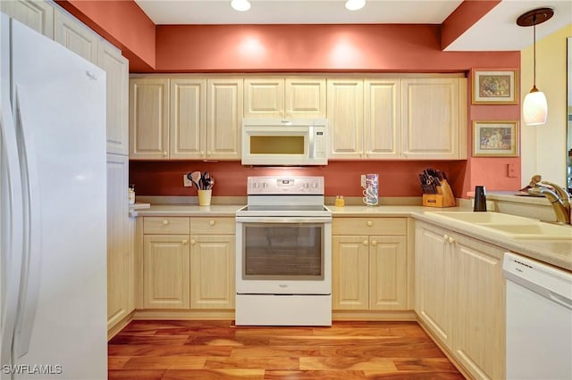 kitchen with hanging light fixtures, sink, white appliances, and light hardwood / wood-style flooring