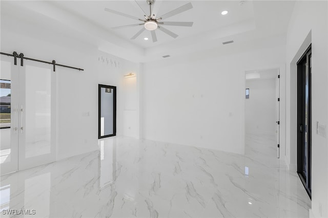 empty room with a raised ceiling, a barn door, and ceiling fan