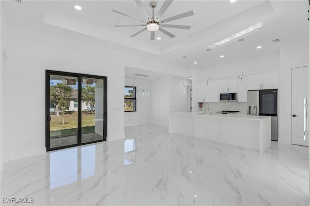 unfurnished living room with sink, ceiling fan, and a tray ceiling