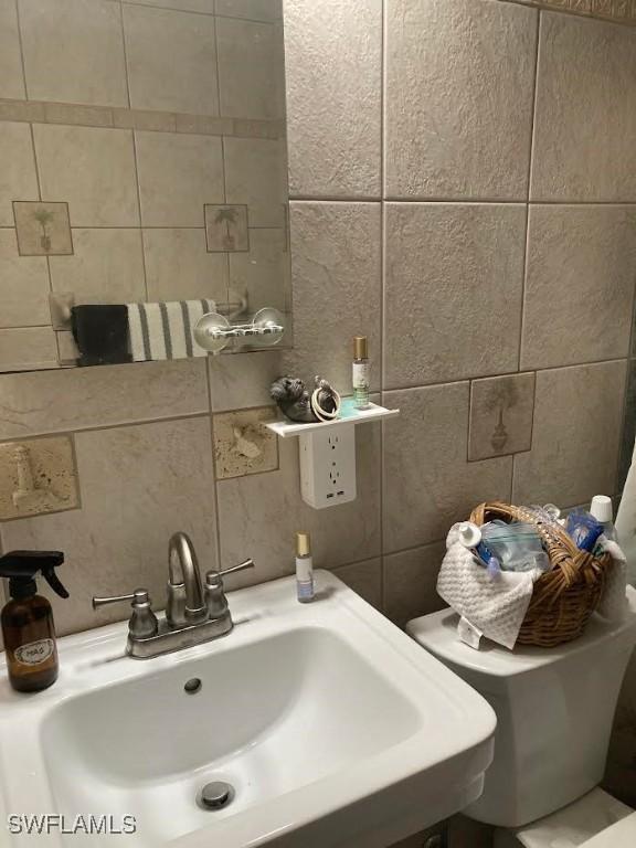 bathroom featuring tasteful backsplash, toilet, sink, and tile walls