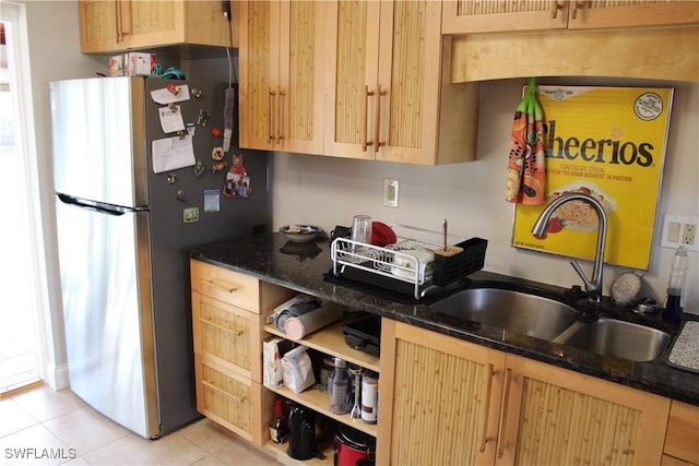 kitchen featuring light tile patterned flooring, light brown cabinetry, sink, dark stone countertops, and stainless steel fridge