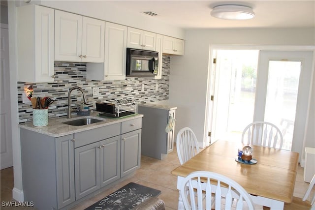 kitchen with white cabinetry, sink, decorative backsplash, light tile patterned floors, and light stone countertops