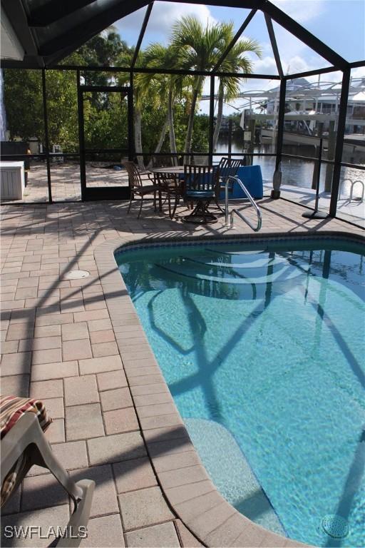 view of swimming pool with a patio, glass enclosure, and a water view