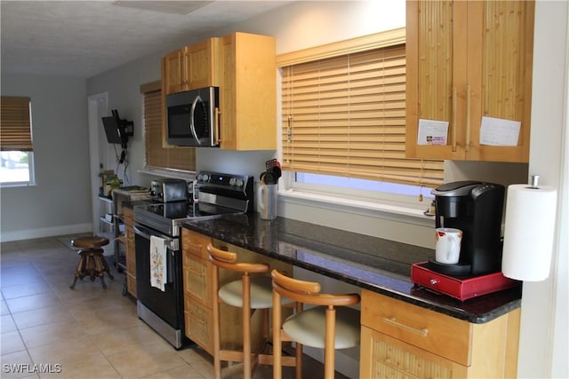 kitchen with dark stone countertops, appliances with stainless steel finishes, a breakfast bar area, and light tile patterned floors