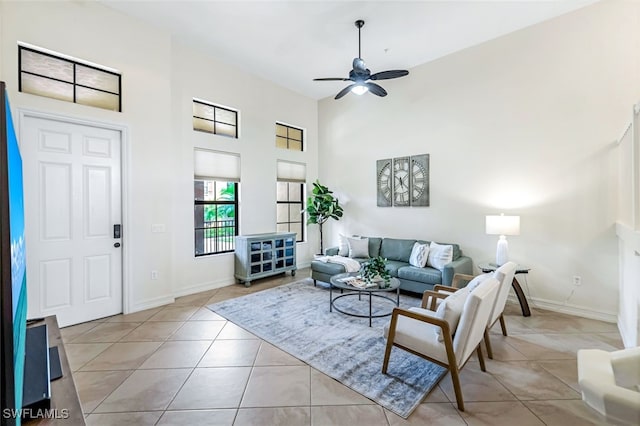 living room with a towering ceiling, light tile patterned floors, baseboards, and a ceiling fan