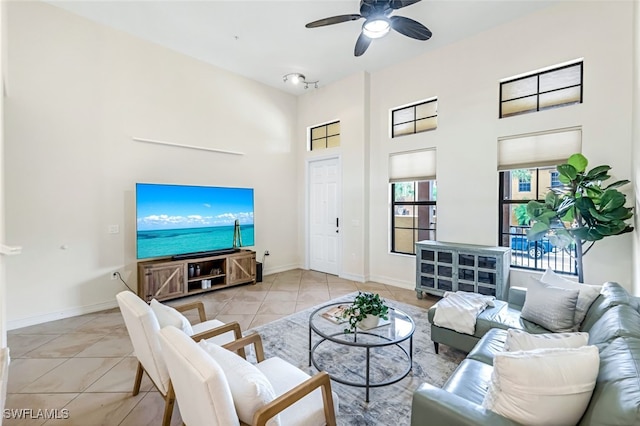 living area featuring light tile patterned floors, a high ceiling, baseboards, and a ceiling fan